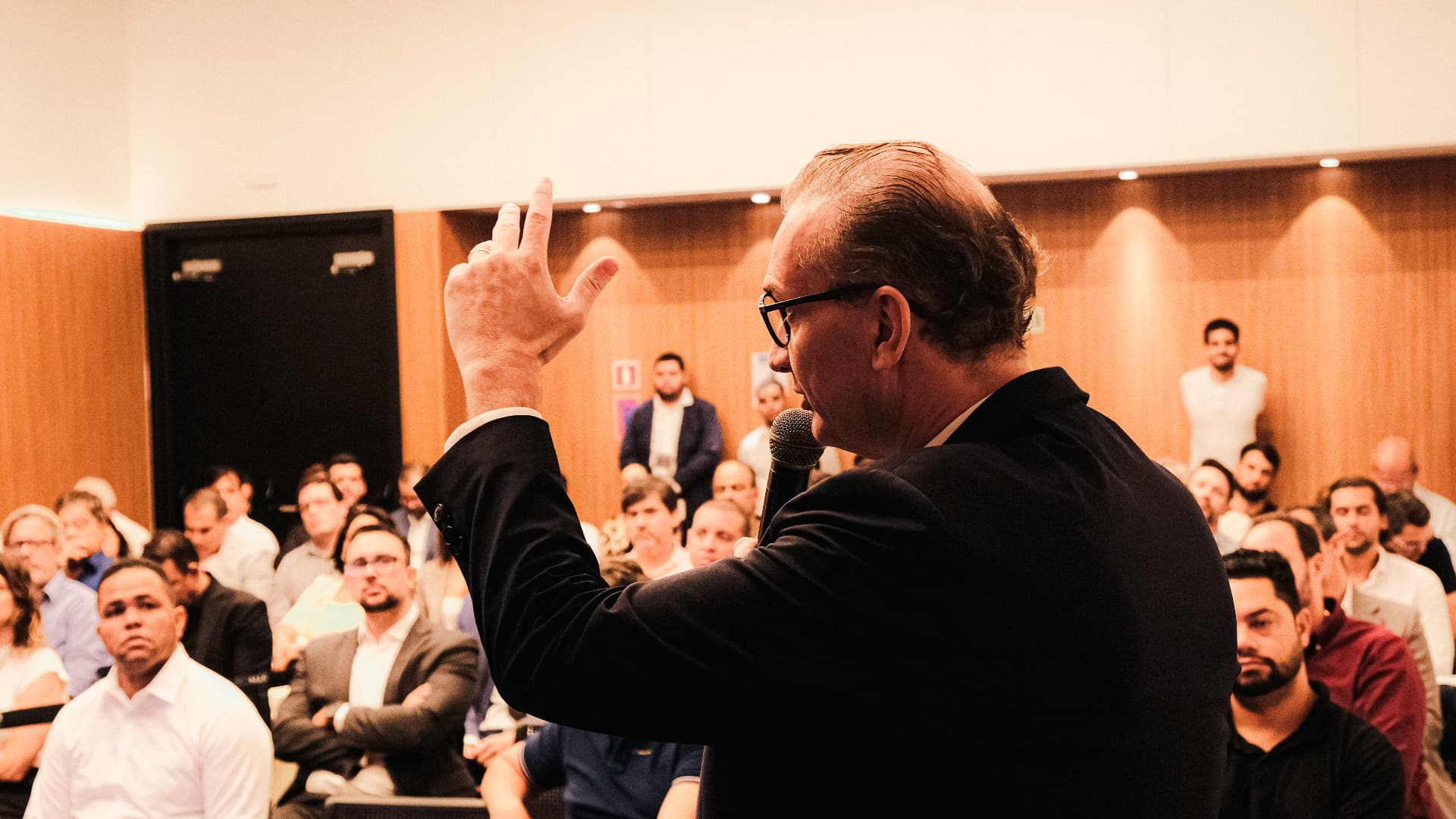 Anthonio Araujo Jr. em pé, falando para uma plateia de executivos